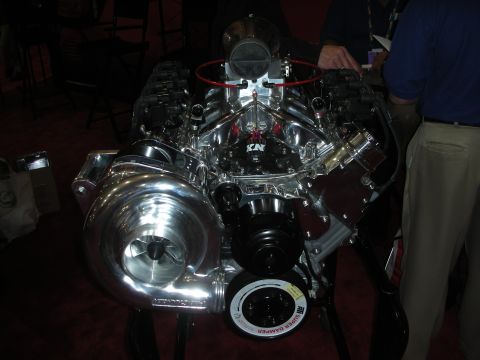 1998 Ford Crown Victoria - Complete chromed supercharged V8 crate engine with K&N air filter on a stand under show lighting.
