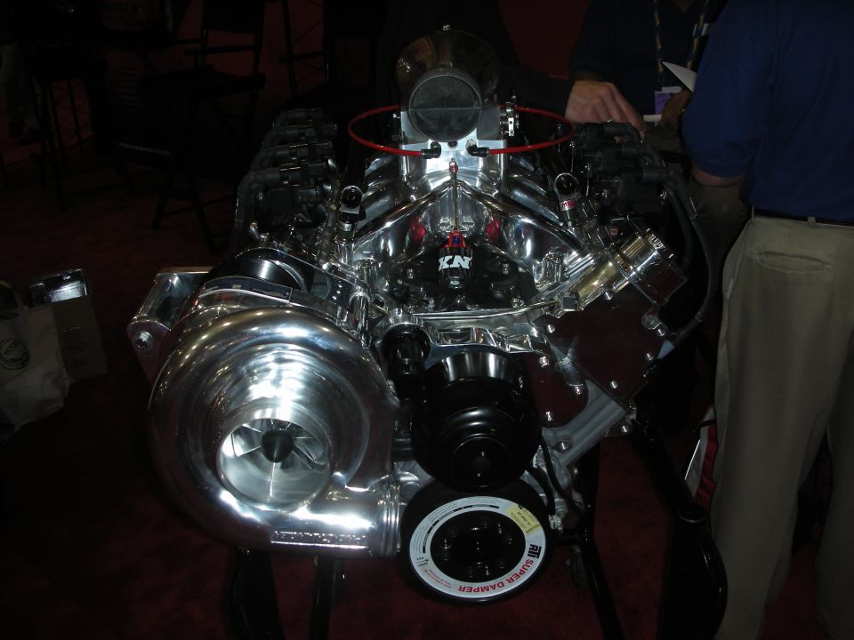 Complete chrome supercharged V8 crate engine displayed under spotlights