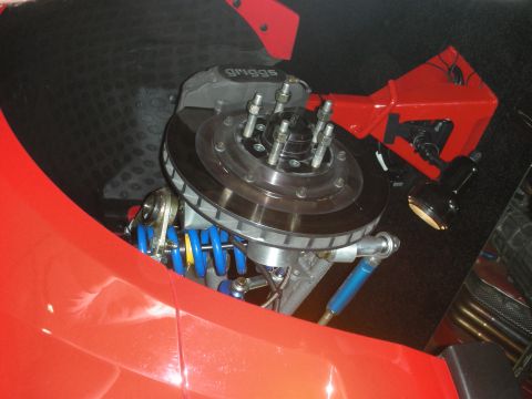 1998 Ford Crown Victoria - Cross-drilled brake rotor with a Griggs caliper and blue coilover spring visible behind a red body panel.