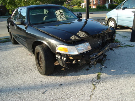 Black 2000 Ford Crown Victoria with significant front-end damage, parked on asphalt