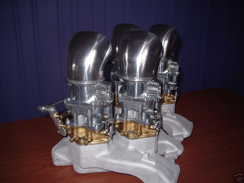 Three two-barrel carburetors with chrome velocity stacks on a polished aluminum intake manifold