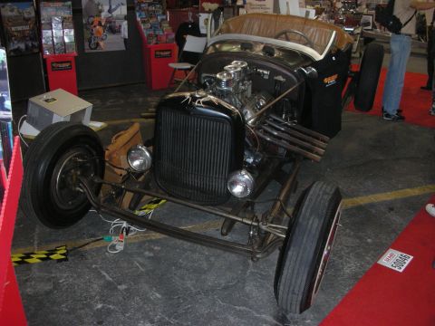 1998 Ford Crown Victoria - Vintage Ford roadster hot rod with bare chassis, exposed engine, and tan tonneau, displayed at an indoor show.