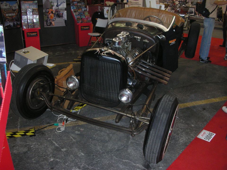 Vintage Ford roadster hot rod chassis with exposed engine at an indoor show