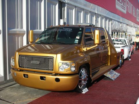 1998 Ford Crown Victoria - Gold custom lowered medium-duty crew-cab hauler truck with chrome wheels displayed outdoors at the SEMA show.