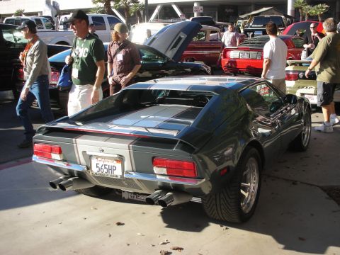 1998 Ford Crown Victoria - Rear three-quarter view of a dark De Tomaso Pantera with silver stripes and a 565HP plate at an outdoor car meet.