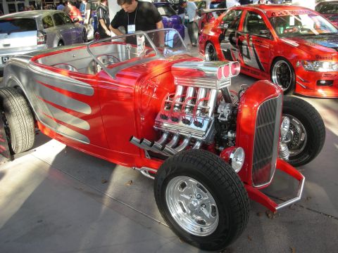 1998 Ford Crown Victoria - Candy-red flamed hot rod roadster with an exposed chrome supercharged engine displayed at an outdoor event.
