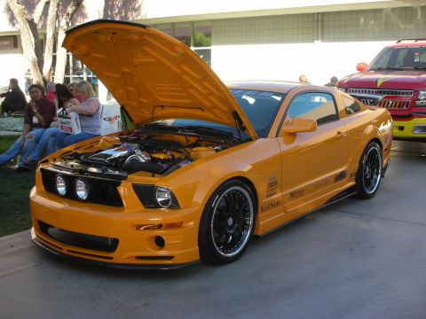 1998 Ford Crown Victoria - Orange custom Mustang coupe with open hood, supercharger, and black multi-spoke wheels displayed outdoors.