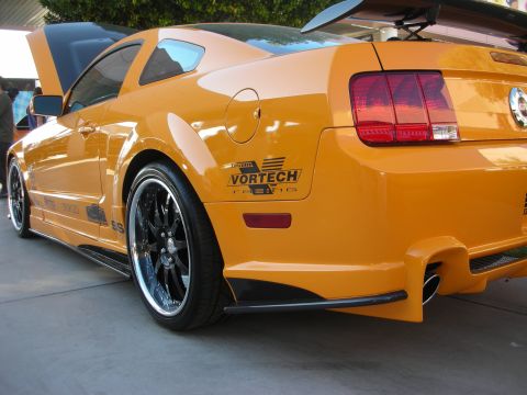 1998 Ford Crown Victoria - Rear quarter of a custom orange Ford Mustang showing a Vortech decal, chrome multi-spoke wheels, and a rear spoiler.