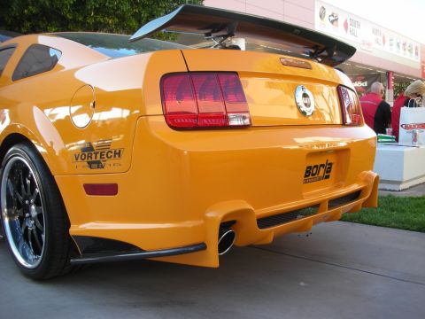 1998 Ford Crown Victoria - Rear view of an orange Ford Mustang with a tall rear wing, custom bumper, and Borla and Vortech decals at a car show.