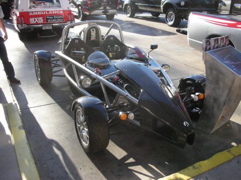 1998 Ford Crown Victoria - Black skeletal track roadster with an exposed tubular chassis, twin seats, and open wheels parked on pavement near an ambulance.