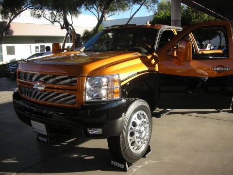 1998 Ford Crown Victoria - Custom orange-and-black Chevrolet dually pickup with a billet grille and polished wheels displayed on Toyo tire stands.