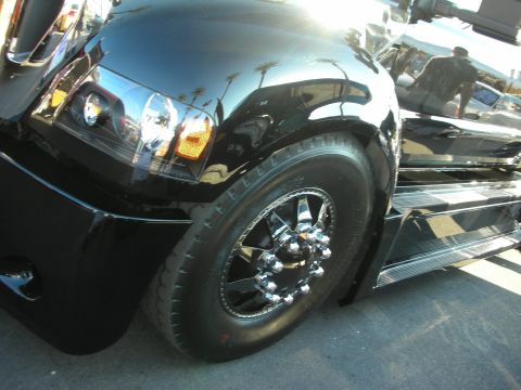 1998 Ford Crown Victoria - Close-up of a glossy black medium-duty truck showing its front fender, headlight, and chrome dual rear wheels with running board.