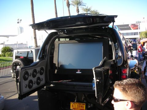 1998 Ford Crown Victoria - Black SUV with open rear hatch revealing a large flip-up video monitor and a panel of speakers in a custom audio build.
