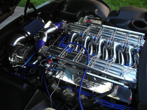 1998 Ford Crown Victoria - Heavily detailed engine bay with a chrome inline-six engine, polished plumbing, blue ignition wires, and a black air intake.