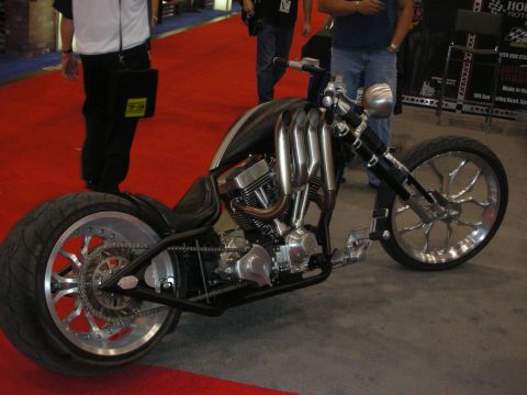 1998 Ford Crown Victoria - Custom chopper motorcycle with a long raked front end, polished cast wheels, and stacked exhaust displayed on red show carpet.
