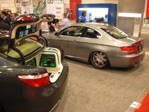 1998 Ford Crown Victoria - Lowered silver BMW coupe beside a gray sedan with an open custom audio trunk on display at an indoor automotive expo.