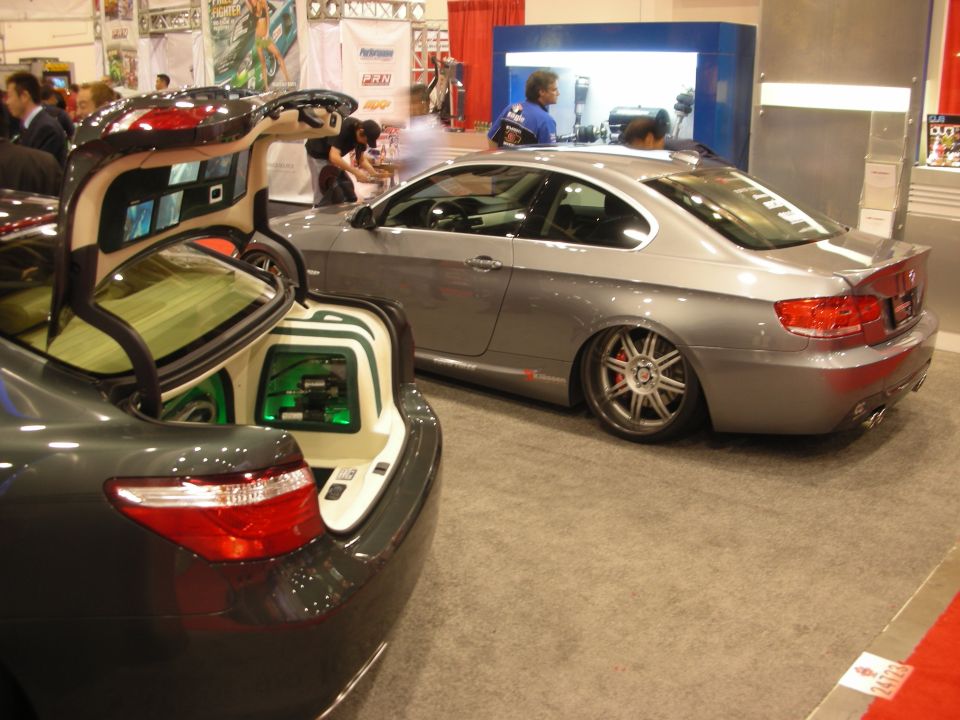 Silver BMW coupe and gray sedan with open audio trunk at indoor show