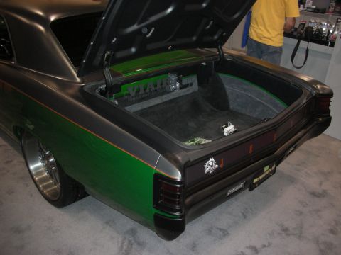 1998 Ford Crown Victoria - Open trunk of a custom green-and-gray muscle car showing a carpeted compartment and slotted taillight panel at an expo.