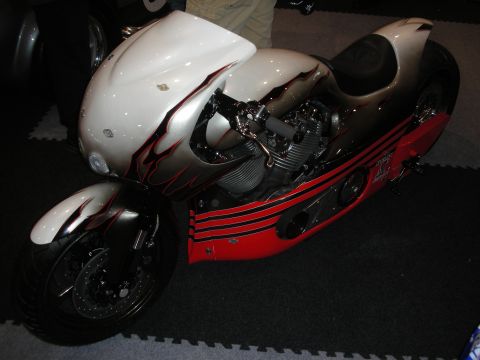 1998 Ford Crown Victoria - Custom motorcycle with full silver bodywork, red flame side panels, and an exposed V-twin engine displayed on foam flooring.