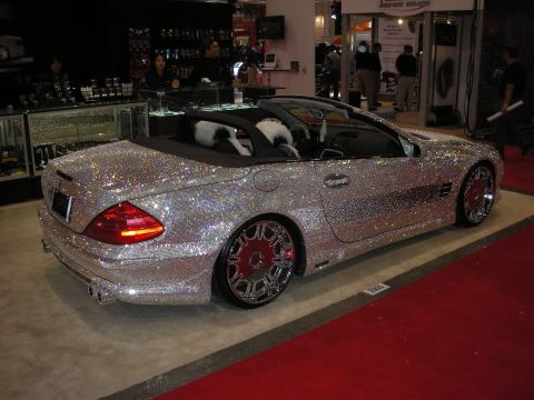 1998 Ford Crown Victoria - silver roadster convertible covered head to toe in sparkling rhinestone-like crystals sits on red carpet at an indoor expo booth.