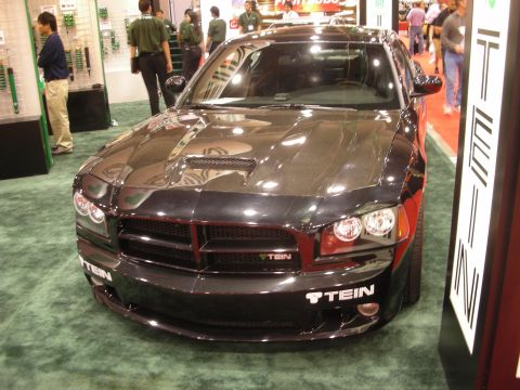 1998 Ford Crown Victoria - Front view of a glossy black four-door sedan with a hood scoop, displayed at a TEIN suspension booth on green carpet.