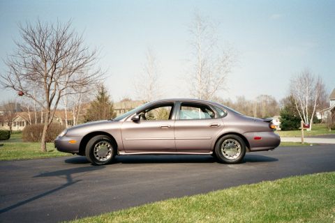 1996 Ford Taurus - A purple 1996 Ford Taurus sedan is parked on a residential driveway on a clear day.