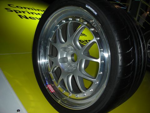 1998 Ford Crown Victoria - close-up of a polished multi-spoke BBS forged alloy wheel mounted with a Michelin tire on a yellow display surface.