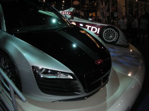 1998 Ford Crown Victoria - silver-and-black mid-engine Audi sports car on a raised display with a TDI Le Mans race car visible behind it.
