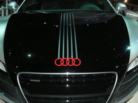1998 Ford Crown Victoria - Front hood of a black Audi showing the red illuminated four-ring emblem and silver vertical racing stripes above the grille.