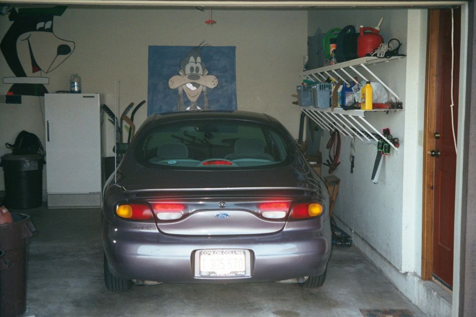 Rear of purple Ford Taurus sedan parked in a garage with Goofy artwork on walls