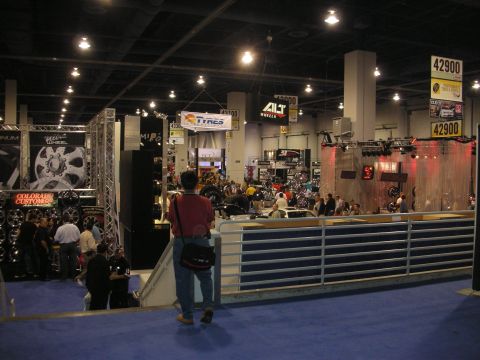 1998 Ford Crown Victoria - person stands at a railing overlooking a crowded indoor trade show floor lined with wheel vendor booths and price signs.