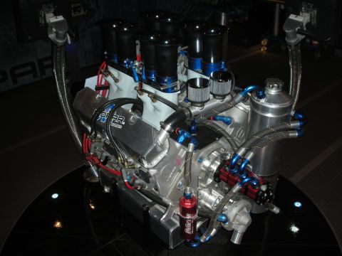 1998 Ford Crown Victoria - Overhead view of a polished aluminum race V8 with eight individual velocity stacks, braided lines, and a red fuel filter on a black stand.