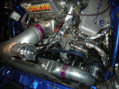 1998 Ford Crown Victoria - Engine bay of a blue car showing a polished Paxton supercharger, intercooler piping, and a Charger-branded valve cover.