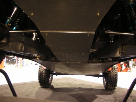 1998 Ford Crown Victoria - Low-angle view of an off-road truck's undercarriage with a flat skid plate, coilover shocks and knobby mud tires at an indoor show.