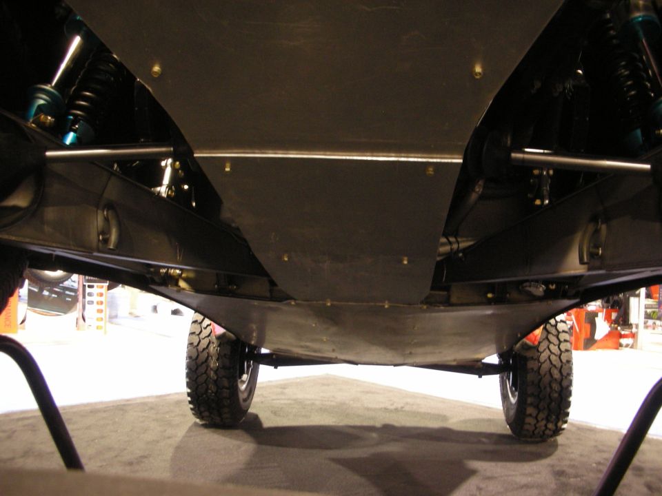 Underside of an off-road vehicle showing skid plate, coilover shocks and mud tires