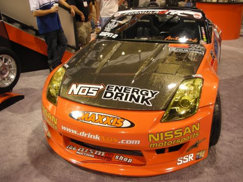 1998 Ford Crown Victoria - Front three-quarter view of an orange Nissan 350Z drift car covered in NOS Energy Drink, Maxxis and Nissan Motorsports sponsor decals.