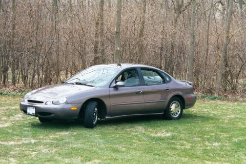 1996 Ford Taurus - Side view of a 1996 Ford Taurus sedan on a grassy area with trees behind it.