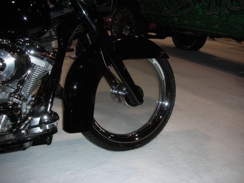 1998 Ford Crown Victoria - Black custom touring motorcycle's front wheel, fender and chrome-trimmed rim displayed on a show floor.