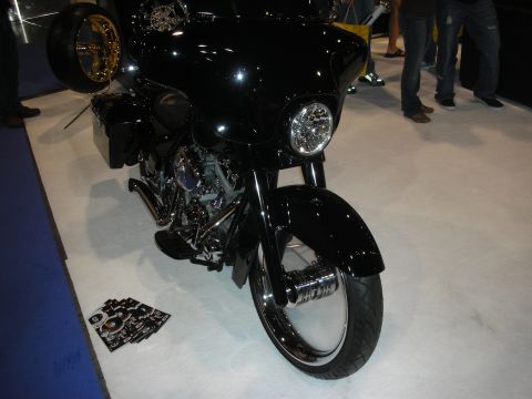 1998 Ford Crown Victoria - Black custom bagger motorcycle with a batwing fairing, chrome headlight and front wheel on a white show floor.