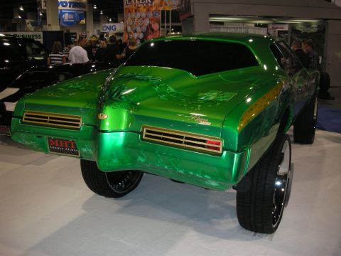 1998 Ford Crown Victoria - Rear three-quarter view of a green candy-painted custom classic coupe lifted on large chrome wheels at an indoor show.