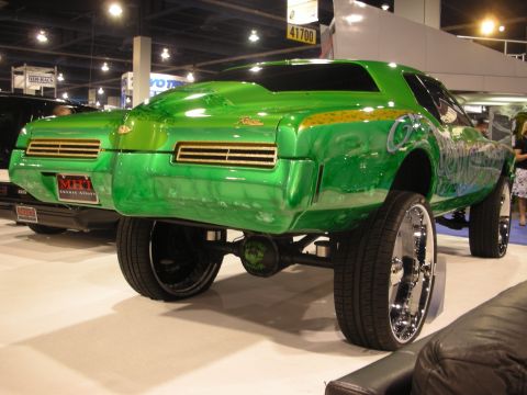 1998 Ford Crown Victoria - Green candy-and-graffiti custom coupe displayed on very tall chrome wire wheels near a Kumho Tires booth.