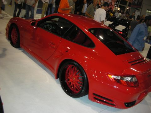 1998 Ford Crown Victoria - Detail of a red Porsche 911's front fender and red-painted multi-spoke show wheel with low-profile tire.