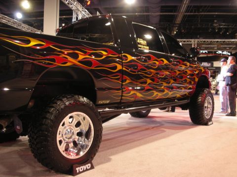 1998 Ford Crown Victoria - Black lifted Dodge Ram pickup with red-and-yellow flame graphics and polished wheels on Toyo tires at an indoor show.