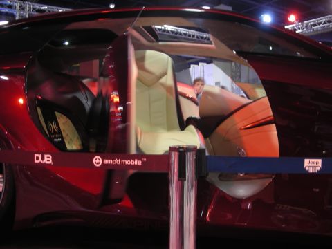 1998 Ford Crown Victoria - cream leather interior of a dark red custom car is visible through its curved side glass behind a roped-off display barrier.