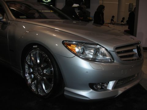 1998 Ford Crown Victoria - front fender, headlight and chrome multi-spoke wheel of a silver Mercedes-Benz coupe are shown at an indoor display.