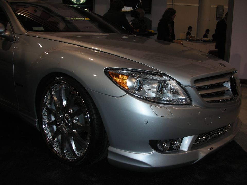 Front corner of a silver Mercedes-Benz coupe with chrome multi-spoke wheels indoors