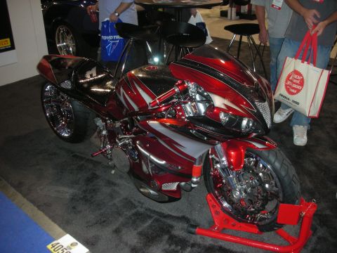 1998 Ford Crown Victoria - custom sportbike with red, black and silver airbrushed bodywork and chrome details sits on a red stand at an indoor show.