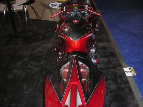 1998 Ford Crown Victoria - rear of a red and black custom sportbike with a pointed tail section is shown from behind on dark show carpet.