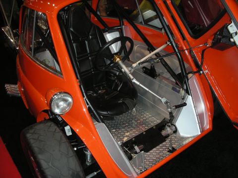 1998 Ford Crown Victoria - orange bubble-style microcar sits with its front door open, revealing a stripped tube-frame interior and steering column.