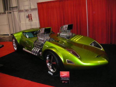 1998 Ford Crown Victoria - bright green custom show car displays two exposed supercharged V8 engines, set against a red curtain backdrop.